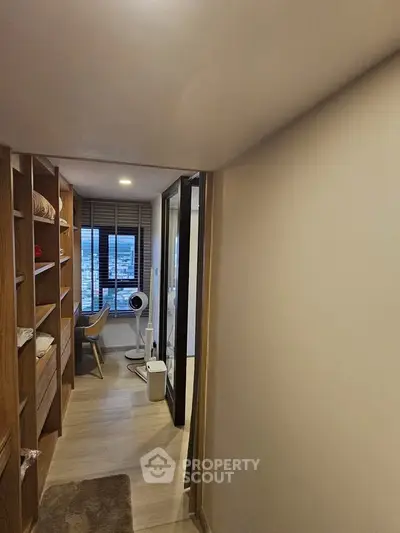Modern apartment hallway leading to a cozy study with city view, featuring wooden shelves and sleek design.