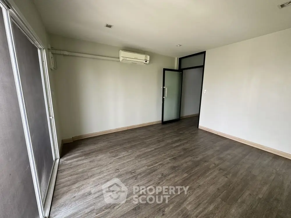Spacious empty room with wooden flooring and air conditioning, perfect for customization.