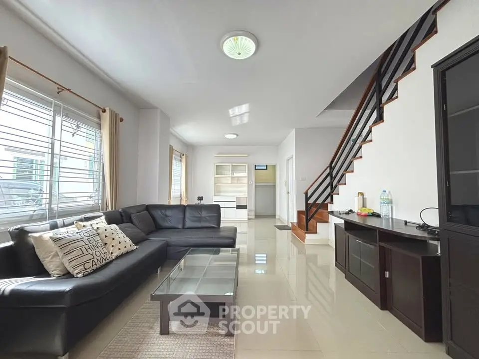 Spacious modern living room with sleek black sofa and elegant staircase in a bright, airy home.