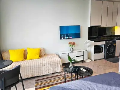 Modern living room with stylish decor, featuring a cozy sofa, wall-mounted TV, and sleek kitchen appliances.