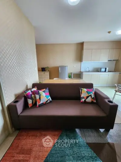 Modern living room with stylish sofa and colorful cushions, open kitchen layout in background.