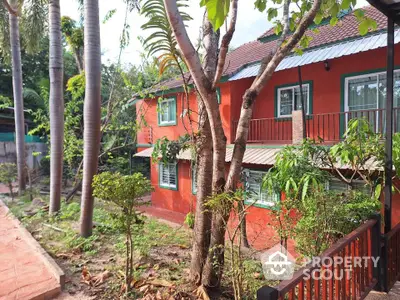 Charming red brick house with lush garden and tall palm trees in serene setting.