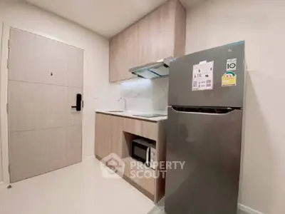 Modern compact kitchen with sleek cabinetry and stainless steel fridge in cozy apartment.