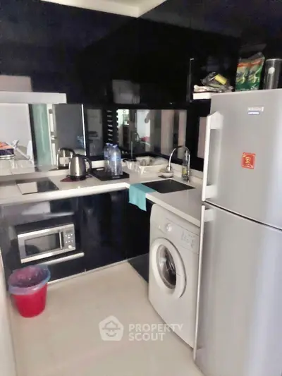 Modern compact kitchen with sleek black cabinets, washing machine, and stainless steel appliances.