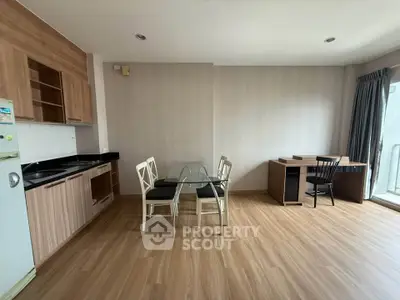Modern open-plan living area with kitchen and study corner, featuring wooden flooring and natural light.