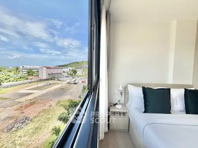 Modern bedroom with large window offering scenic view of urban landscape and greenery.