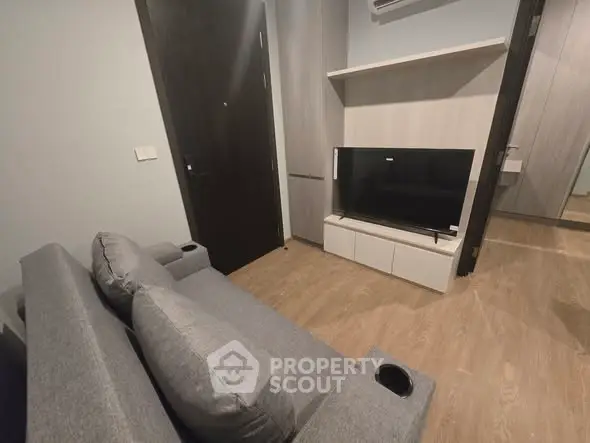 Modern living room with sleek grey sofa and flat-screen TV in stylish apartment.