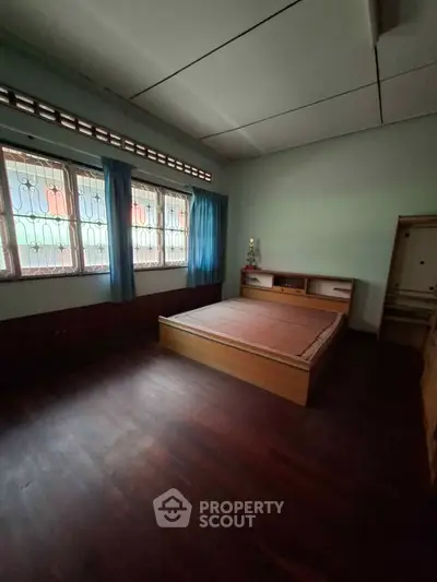 Spacious bedroom with wooden flooring and large windows in a cozy home.