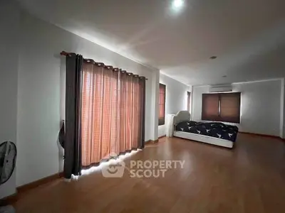 Spacious bedroom with wooden flooring and large windows for natural light.