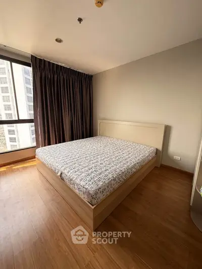 Spacious bedroom with large window and modern wooden flooring in a high-rise apartment.
