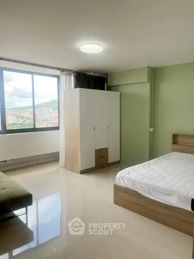 Spacious bedroom with large window offering stunning city views, modern furnishings, and ample natural light.