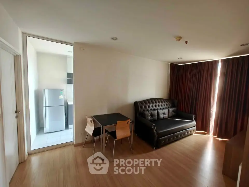 Modern living room with stylish sofa and dining area, adjacent to a kitchen with a fridge.
