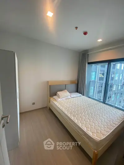 Modern bedroom with large window and minimalist decor in urban apartment.