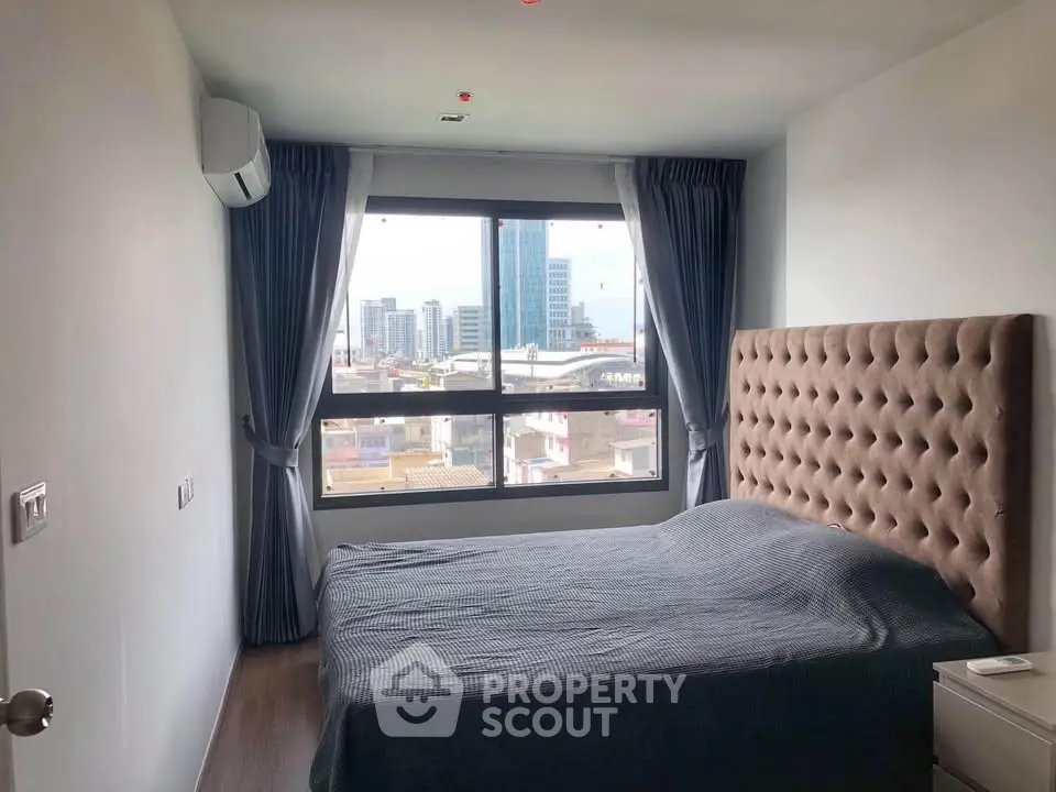 Modern bedroom with city view, featuring plush headboard and large window for natural light.