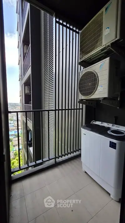 Modern apartment balcony with air conditioning units and washing machine, offering a city view.