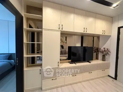 Modern living room with built-in storage and TV, adjacent to a cozy bedroom.