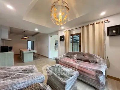 Spacious living room with modern lighting and open kitchen layout, featuring wrapped furniture for protection.