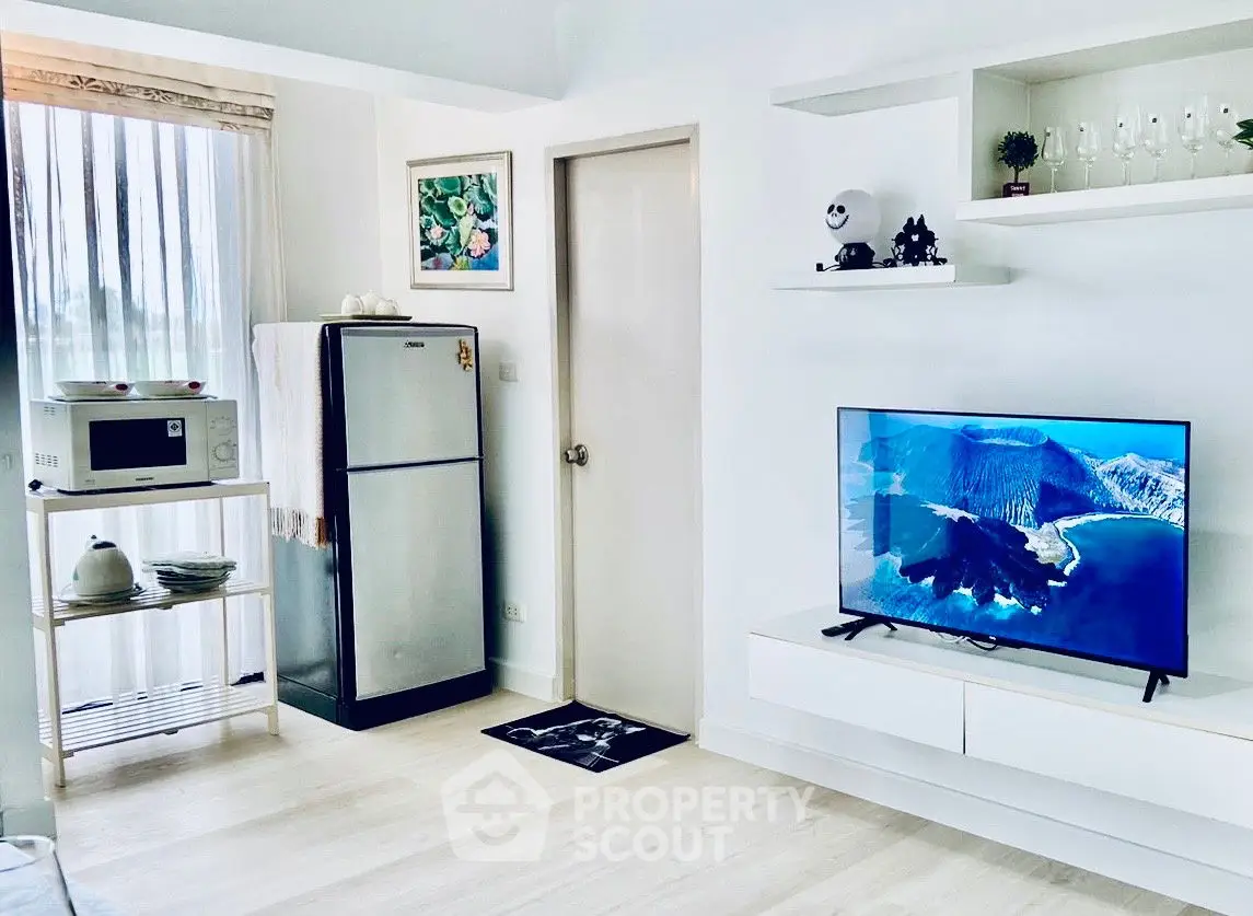 Modern living room with sleek TV setup and compact kitchen appliances.
