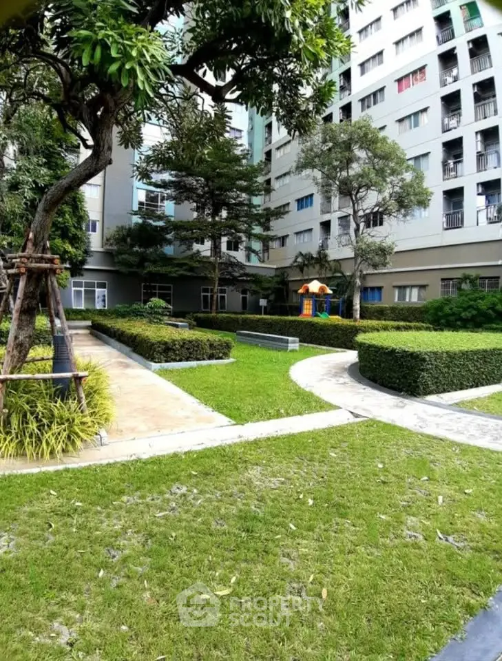 Lush garden area in modern residential complex with walking paths and playground.