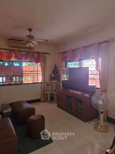 Cozy living room with large windows and elegant curtains, featuring a ceiling fan and entertainment center.