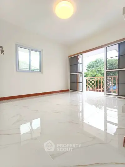 Spacious bright room with glossy marble flooring and large windows opening to a balcony with greenery view.