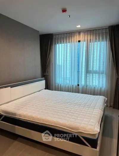 Spacious bedroom with large windows allowing ample natural light, complemented by elegant drapery and a comfortable queen-sized bed.