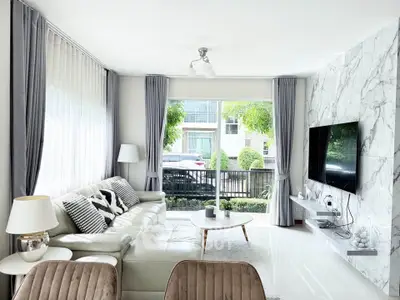 Modern living room with large windows, elegant decor, and a wall-mounted TV, offering a bright and inviting atmosphere.