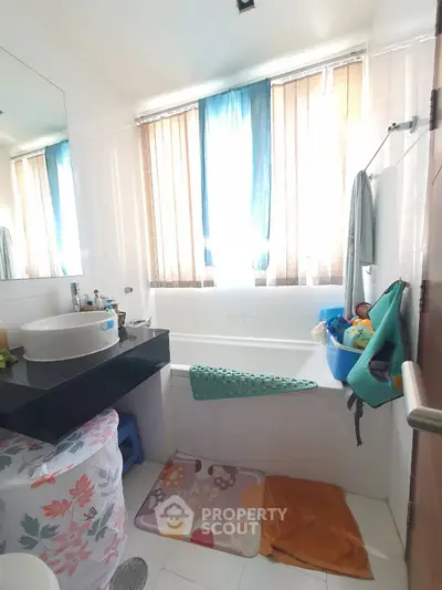 Bright bathroom with bathtub and modern sink, featuring colorful decor and ample natural light.
