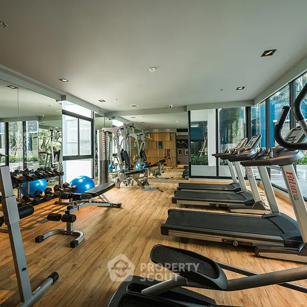 Modern gym with state-of-the-art equipment and large windows in luxury apartment complex.