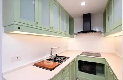 Modern kitchen with green cabinets, sleek countertops, and built-in appliances in a compact layout.