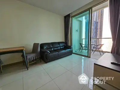 Spacious living room with gleaming tiled floors, comfortable leather sofa, and access to a sunlit balcony perfect for relaxation and entertaining guests.