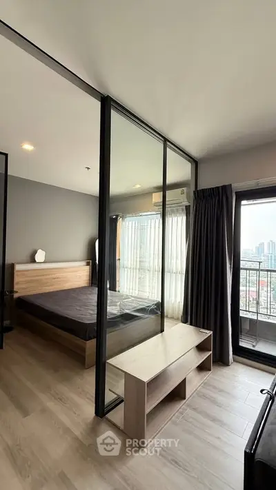 Modern bedroom with glass partition and city view balcony in high-rise apartment.