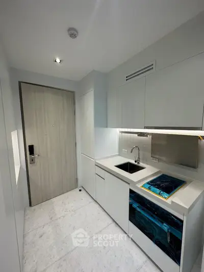 Modern compact kitchen with sleek white cabinetry and built-in appliances in a contemporary apartment.