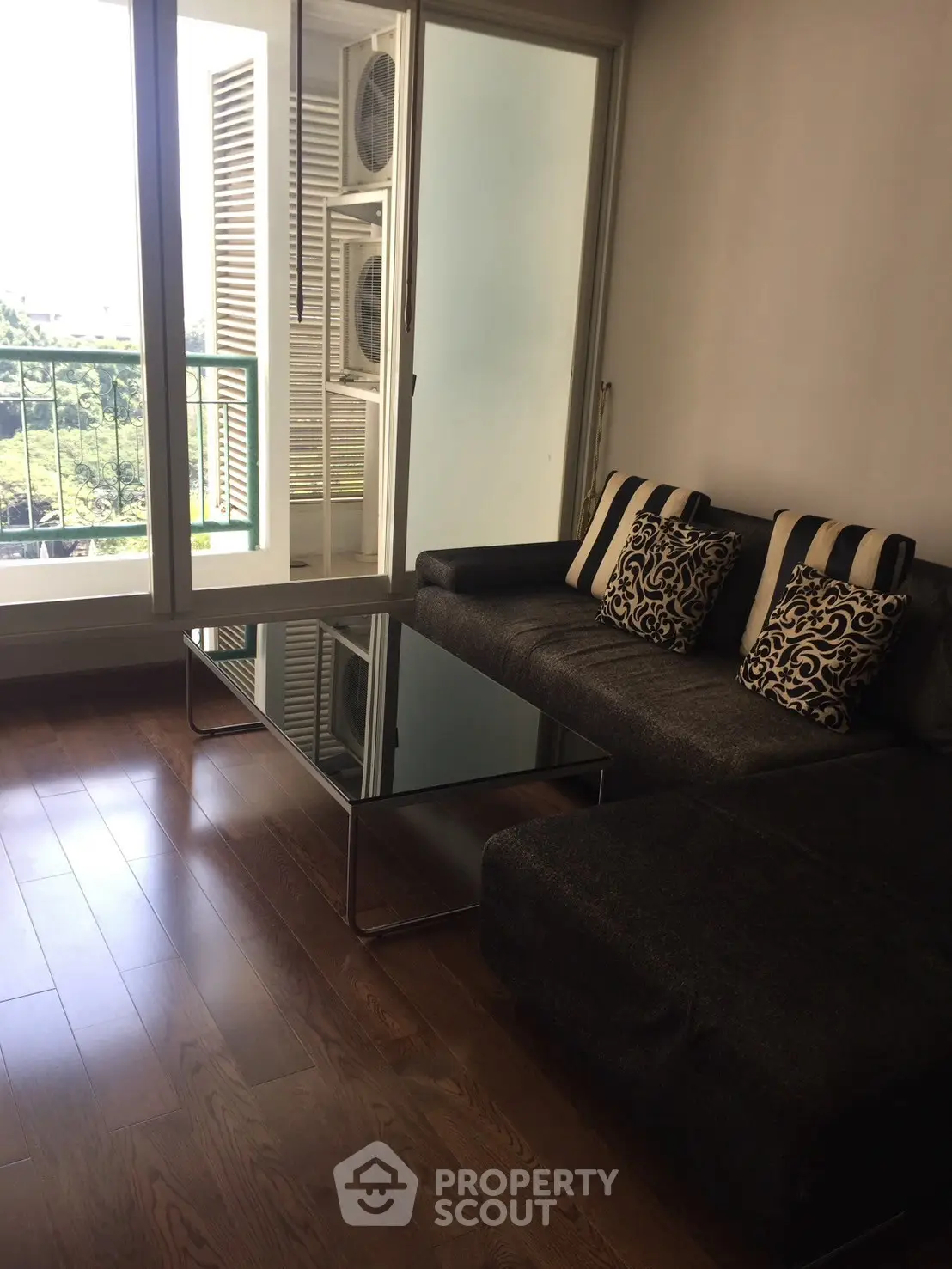 Modern living room with stylish sofa and glass coffee table, featuring a balcony with a scenic view.