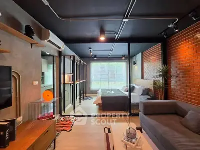 Modern open-plan living room with stylish decor and cozy bedroom view, featuring exposed brick wall and sleek furnishings.