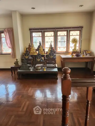 Spacious room with wooden flooring and decorative statues near large windows.