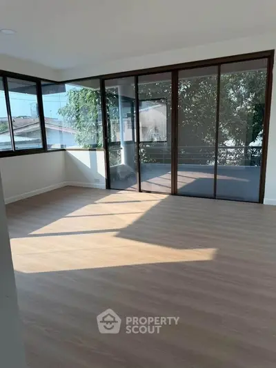 Spacious sunlit room with large windows and wooden flooring, perfect for a modern living space.