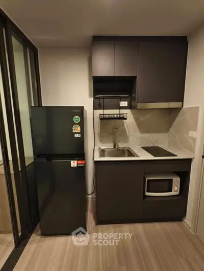 Modern compact kitchen with sleek black cabinets, fridge, microwave, and electric stove in a stylish apartment.