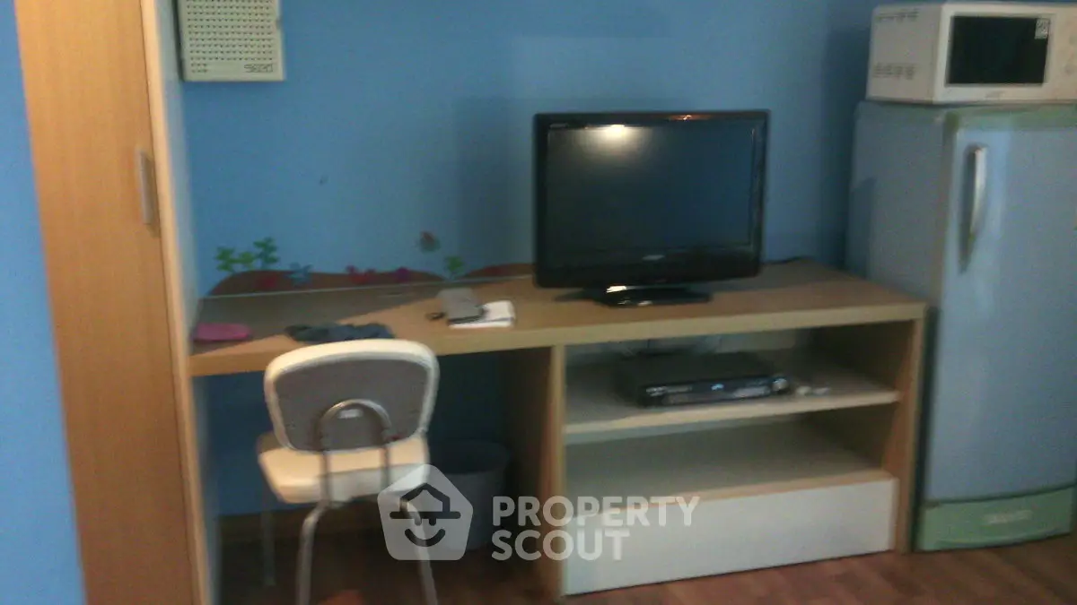 Cozy study area with desk, chair, TV, and microwave in a compact space.