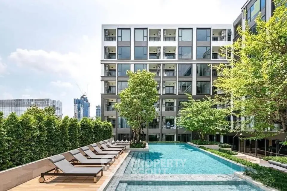 Modern apartment building with a luxurious outdoor pool and sun loungers, surrounded by lush greenery.
