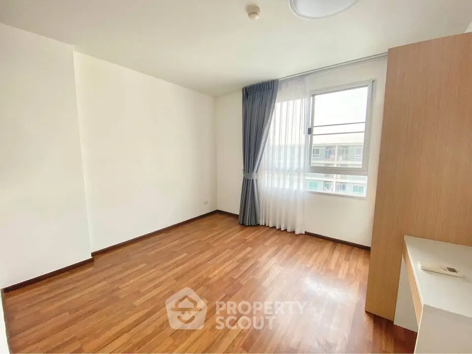 Spacious empty bedroom with wooden flooring and large window.