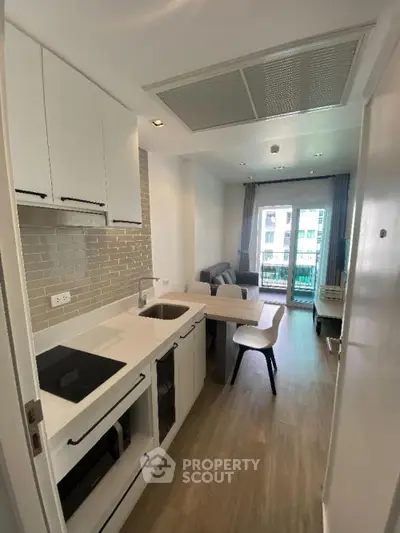Modern kitchen with sleek white cabinetry and built-in appliances seamlessly opens to a cozy living area, leading to a sunlit balcony.