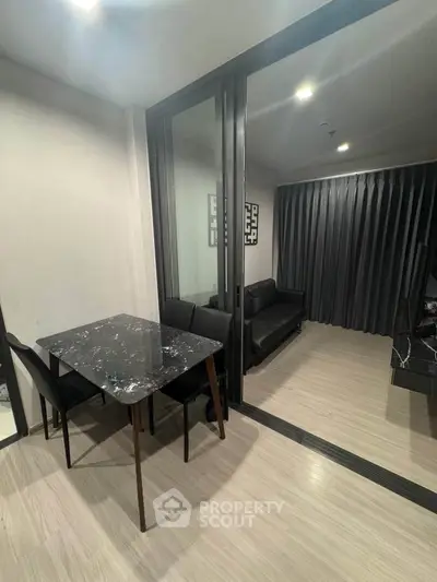 Modern apartment with sleek dining area and cozy living room, featuring elegant black furnishings and floor-to-ceiling curtains.