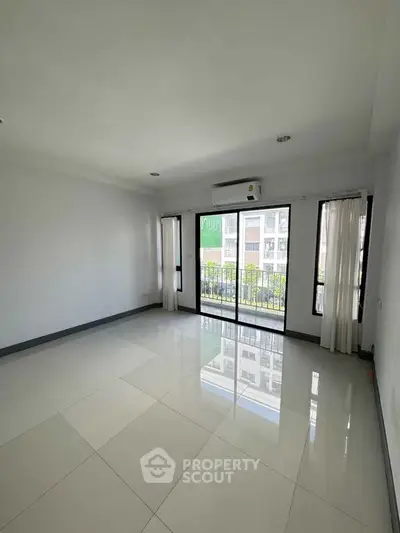 Spacious empty living room with large windows and balcony access in modern apartment.