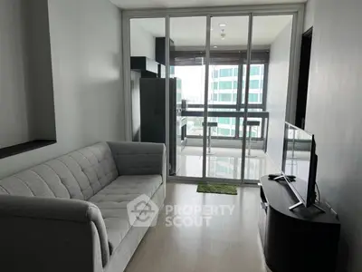 Modern living room with sleek sofa and TV, leading to a bright balcony with city views.