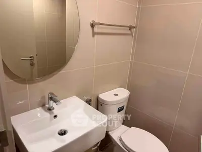 Modern bathroom with sleek fixtures and neutral tiles, featuring a round mirror and compact sink.