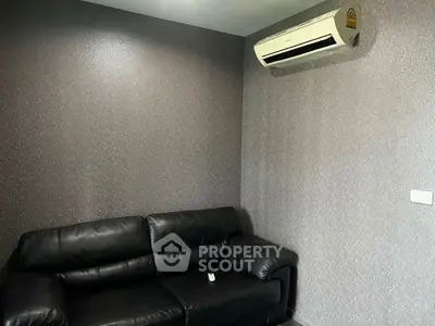 Modern living room with sleek black leather sofa and wall-mounted air conditioner.