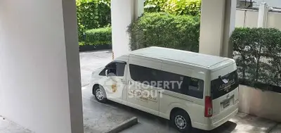 Modern building entrance with branded shuttle van parked, lush greenery surrounds the area.
