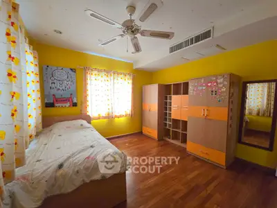 Bright and cozy bedroom with wooden flooring and vibrant yellow walls, featuring ample storage and natural light.