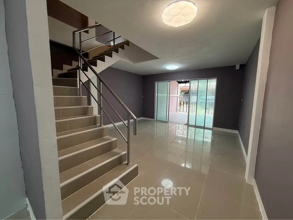 Spacious modern living room with sleek staircase and large sliding glass doors.